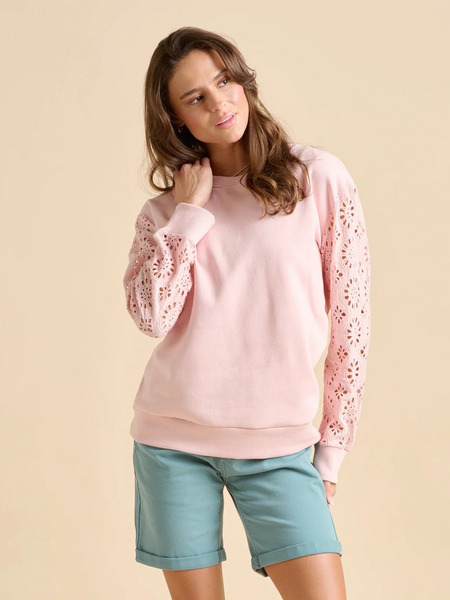 Woman wearing a pink sweater with lace sleeves and light blue shorts on a beige background