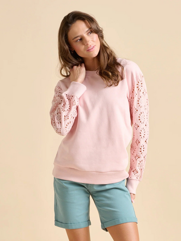 Woman wearing a pink sweater with lace sleeves and light blue shorts on a beige background
