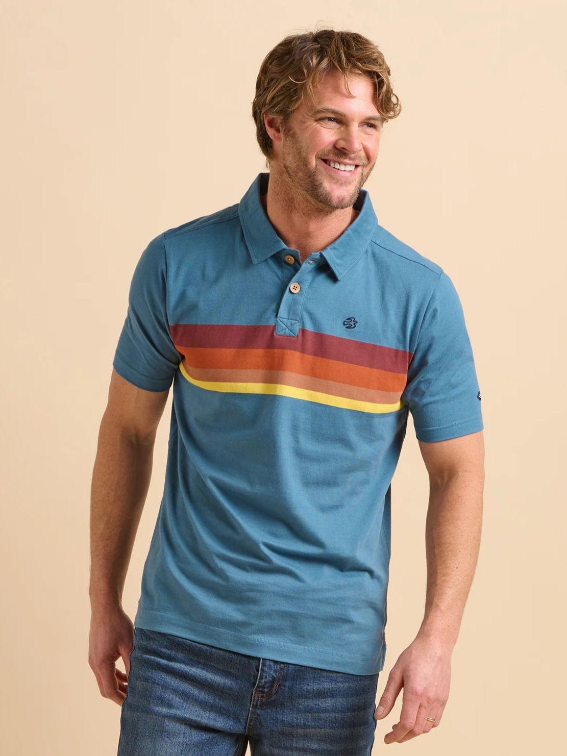 Man wearing a blue polo shirt with colorful stripes and jeans on a beige background